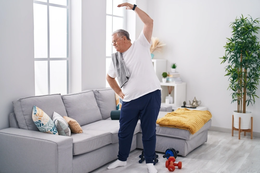 Paziente che esegue esercizi di riabilitazione a casa, integrandoli nella routine quotidiana.