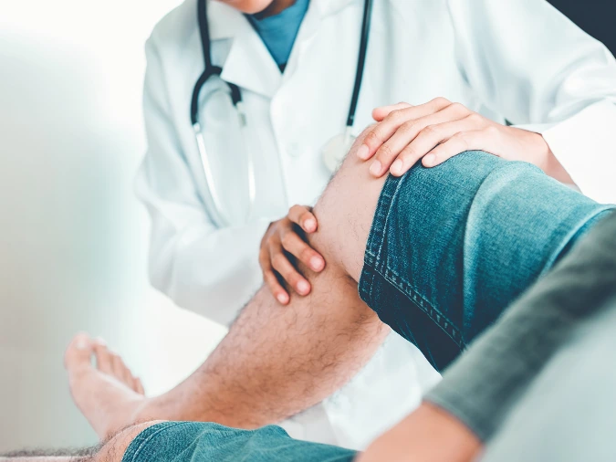 Medico ortopedico che esamina un ginocchio di un paziente.