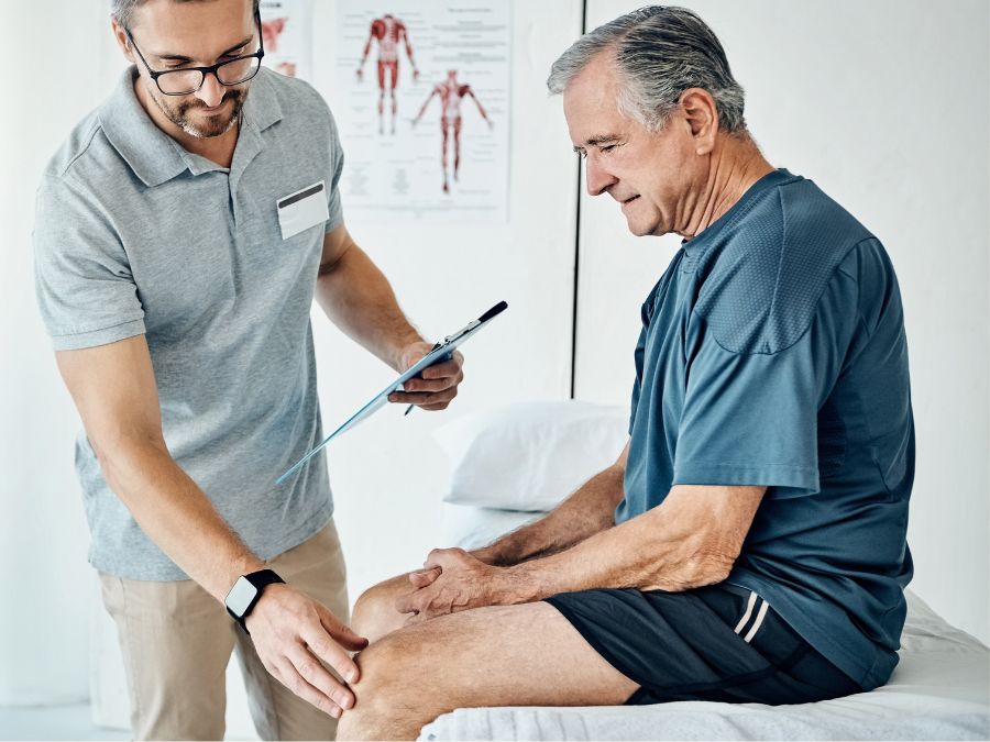 Ortopedico aiuta un paziente anziano nella riabilitazione dopo protesi al ginocchio.