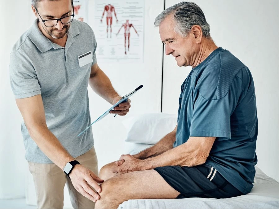 Ortopedico aiuta un paziente anziano nella riabilitazione dopo protesi al ginocchio.